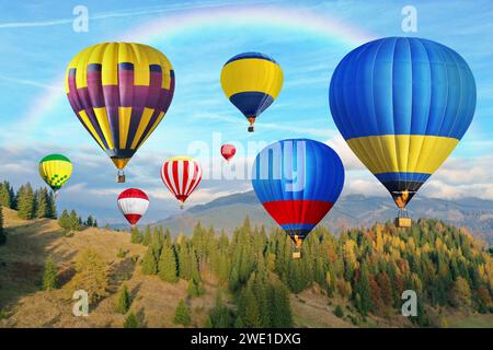 Helle Heißluftballons fliegen in den Himmel mit Regenbogen über den Berg Stockfoto