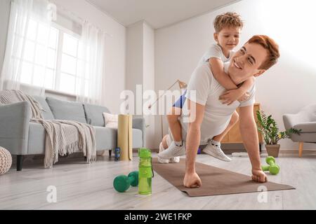 Sportlicher junger Mann mit seinem kleinen Sohn, der zu Hause Plank macht Stockfoto