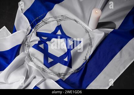 Flagge Israels mit Stacheldraht und brennender Kerze auf schwarzem Hintergrund. Internationaler Holocaust-Gedenktag Stockfoto