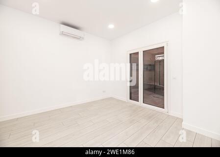 Ein leeres, weißes Zimmer in einem Haus im Loft-Stil mit einer Eingangstür aus Aluminium und Glas und einer Klimaanlage an der Wand Stockfoto