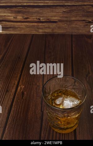 Ein durchsichtiges Glas, gefüllt mit einer bernsteinfarbenen Flüssigkeit und etwas Eis Stockfoto