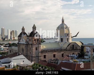 Die bezaubernde Kirche San Pedro Claver in Cartagena, Kolumbien, wurde im Glanz des Abends mit einem anmutigen Vogel gebadet, der gegen den hellen Himmel schwingt. Stockfoto