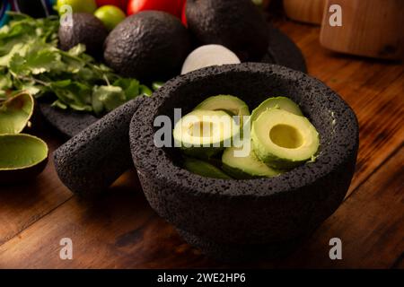 Grundlegende Zutaten für die Zubereitung von Avocado-Dip, bekannt als Guacamole, hergestellt in einer vulkanischen Stein-Molcajete, einer sehr beliebten Avocado-Sauce. Traditionelles Rezept Stockfoto