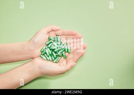 Viele Vitaminkapseln werden auf grünem Hintergrund in die Handfläche einer Frau gelegt. Leerzeichen für Text und Design. Das Konzept des Vitaminsupplems Stockfoto