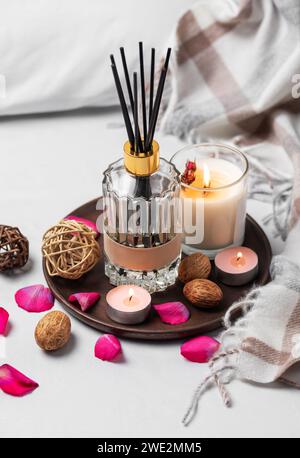 Gemütliches Zuhause. Flüssiger Duft in Glasflasche und Duftkerze auf Tablett. Stockfoto