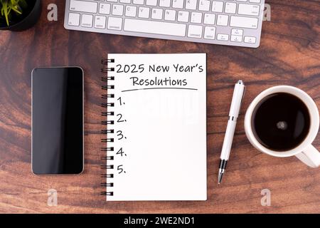 Neujahrsvorsätze 2025 Text auf Notizblock, Stift, Smartphone, Kaffee auf Holzschreibtisch Stockfoto