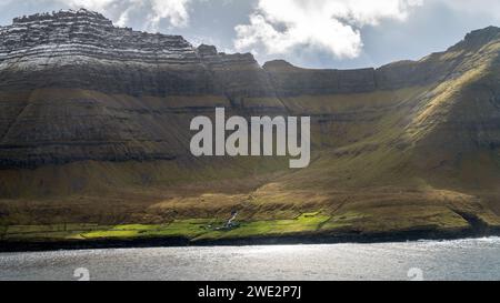 Auf den Färöern liegt ein kleines Dorf inmitten einer dramatischen Landschaft. Stolz erheben sich Klippen, die vom Nordatlantik erschlagen werden. Stockfoto