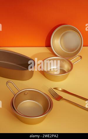 Vor dem farbigen Hintergrund, Set aus goldenen Töpfen und Tabletts aus Edelstahl mit Messer und Gabel verziert. Pop-Art-Design. Stockfoto