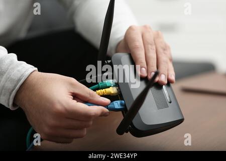 Mann, der Kabel in den WLAN-Router an einem Holztisch drinnen steckt, Nahaufnahme Stockfoto