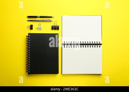 Notizbücher, Stifte und Büroklammern auf gelbem Hintergrund, flach gelegt Stockfoto