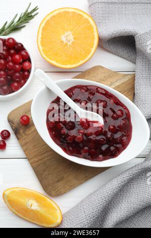 Leckere Preiselbeersauce in Schüssel, frische Beeren und Orangenscheiben auf weißem Holztisch, flach gelegt Stockfoto