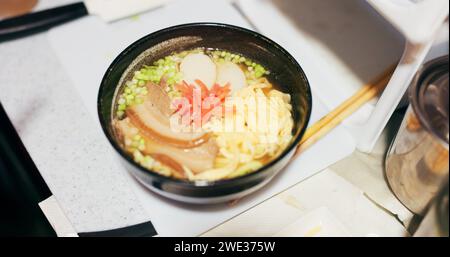 Ramen-Essen, Teller und Tisch im Restaurant mit Person, Händen und Ingwer mit Nahaufnahme für japanische Küche. Niboshi Schüssel, Essstäbchen und Schweinefleisch für Diät Stockfoto