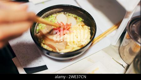 Ramen-Essen, Teller und Tisch im Restaurant mit Person, Händen und Ingwer mit Nahaufnahme für japanische Küche. Niboshi Schüssel, Essstäbchen und Schweinefleisch für Diät Stockfoto