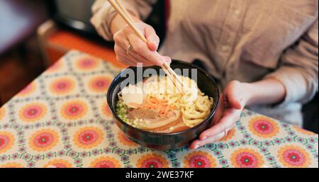 Ramen-Essen, Teller und Tisch im Restaurant mit Person, Händen und Ingwer mit Nahaufnahme für japanische Küche. Niboshi Schüssel, Essstäbchen und Schweinefleisch für Diät Stockfoto