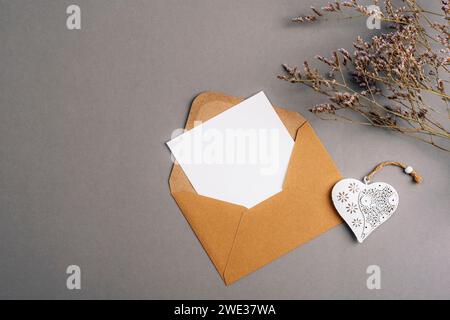 Umschlag mit leerer Karte, Vintage-Spielzeugherz und Blumen auf grauem Hintergrund. Valentinstag-Konzept, Draufsicht, flache Ladefläche, Mockup. Stockfoto