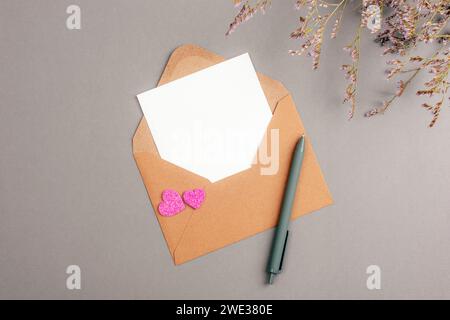 Umschlag mit leerer Karte, Herzen und Blumen auf grauem Hintergrund. Valentinstag-Konzept, Draufsicht, flache Ladefläche, Mockup. Stockfoto
