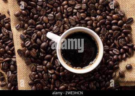 Tasse Kaffee mit Bohnen auf Jute-Hintergrund Stockfoto