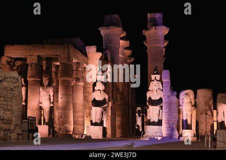 Beleuchteter Luxor-Tempel. Der peristilvolle Innenhof von Ramesses II. Mit zwei sitzenden Granitstatuen und der Prozessionskolonnade von Amenhotep III Stockfoto