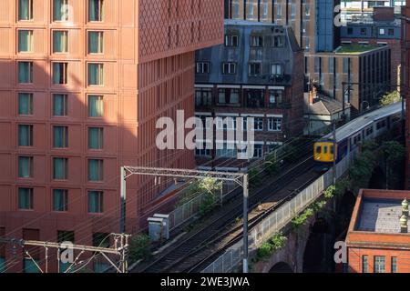 Ein Zug, der auf einer elektrifizierten Strecke über einem viktorianischen Viadukt neben dem Maldron Hotel in Manchester, Großbritannien fährt Stockfoto