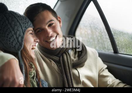 Liebe, regnete und Pärchen im Auto für einen Roadtrip zusammen, lacht über ein Date für Reisen, Urlaub oder Romantik. Lächeln, Winter oder Wetter mit Mann und Frau Stockfoto