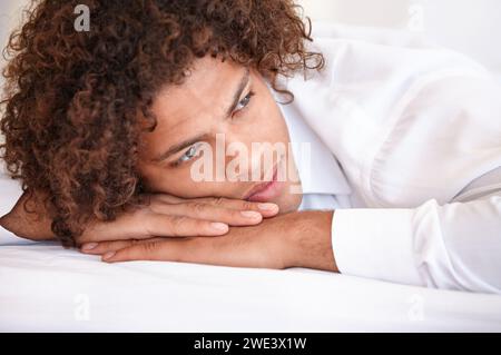 Mann, nachdenklich und entspannend im Bett am Wochenende, faul und bequem am Morgen zu Hause. Männliche Person, friedlich und tagträumend, während sie im Schlafzimmer ausruht Stockfoto