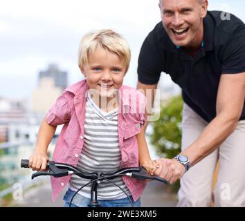Fahrrad, Porträt und Vater mit Kind auf einer Straße, um Hilfe zu leisten, zu lernen oder gemeinsam im Freien zu fahren. Liebe, Familie oder Eltern mit Kind in einer Straße für Stockfoto