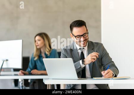 Junger Geschäftsmann mit Laptop im Büro. Der Manager denkt über erfolgreiche finanzielle Ideen nach. Stockfoto