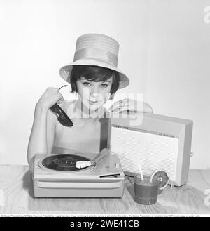 Lifestyle der 1960er Jahre. Eine junge Frau mit einem Philips Radio und einem Grammophon, wie es im Sommer aussehen könnte. Der Sommerhut, die Sonnenbrille und das kühle Getränkeglas auf dem Bild sind hinzugefügt, um das richtige Sommergefühl im Studio zu bekommen. 1962 Kristoffersson Ref. 374A Stockfoto