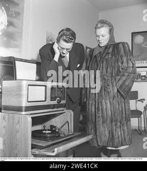 In den 1940er Jahren Ein junges Paar bewundert den Klang des neuen Radiogrammtelefons der Firma Tandberg in einem Geschäft. Das Radio sendet und auf dem Sie Grammophon-Aufnahmen wiedergeben können. Dieses Modell des Plattenspielers konnte mit mehreren Discs geladen werden, die nacheinander automatisch abgespielt wurden. 1949 Kristoffersson Ref. AU41-9 Stockfoto