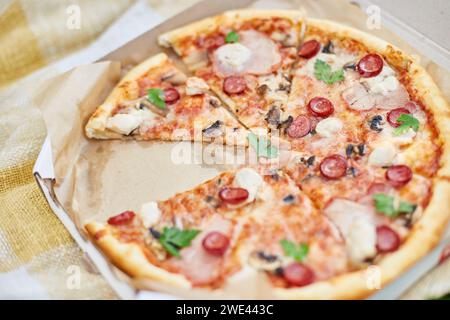 Eine frisch gebackene Pizza mit Tomaten, Käse, Pilzen und Kräutern fehlen zwei Scheiben, was eine gemeinsame Mahlzeit bei einem Picknick im Freien nahe legt. Stockfoto