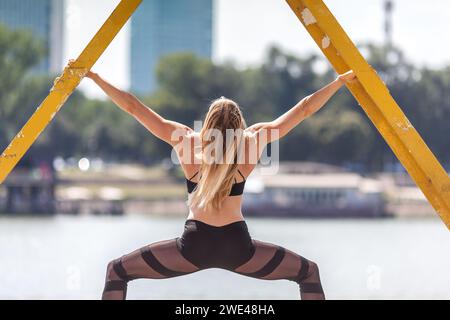 Rückansicht einer fitten muskulösen Frau, die auf einem alten Metallkran trainiert Stockfoto