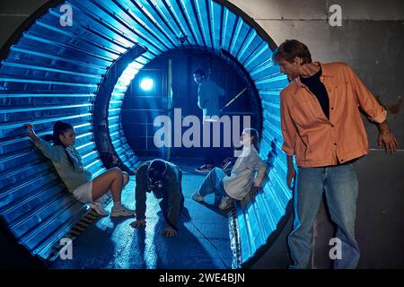 Verschiedene Gruppen von Freunden, die an aufregenden Abenteuern im Quest Room teilnehmen, im Tunnel mit blauem Licht Stockfoto