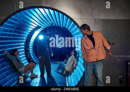 Interrassische Gruppe von Freunden, die an aufregenden Abenteuern im Quest Room teilnehmen, in einem Tunnel mit blauem Licht Stockfoto