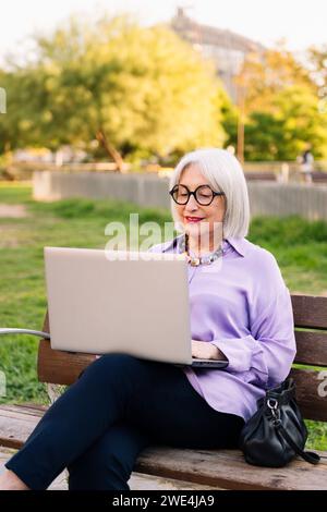 Ältere Frau mit Brille, die draußen einen Laptop benutzt Stockfoto