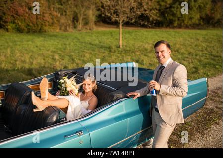 Lustige, ungewöhnliche, stilvolle, originelle Fotos mit Rollenumkehr eines jungen, attraktiven Brautpaares mit wunderschönen Veteranenautos in der Natur. Stockfoto