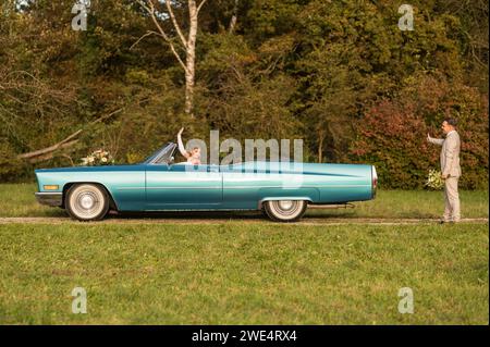 Lustige, ungewöhnliche, stilvolle, originelle Fotos mit Rollenumkehr eines jungen, attraktiven Brautpaares mit wunderschönen Veteranenautos in der Natur. Stockfoto