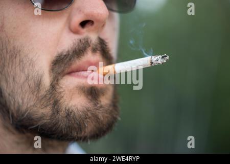 Nahaufnahme eines bärtigen Mannes in Sonnenbrille, der Zigarette raucht. Stockfoto