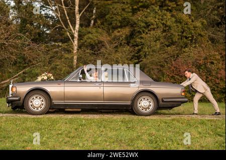 Lustige, ungewöhnliche, stilvolle, originelle Fotos mit Rollenumkehr eines jungen, attraktiven Brautpaares mit wunderschönen Veteranenautos in der Natur. Stockfoto