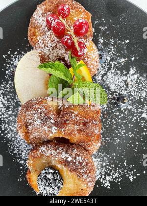 Apfelfritter auf dunklem Teller mit Zucker und Früchten. Stockfoto