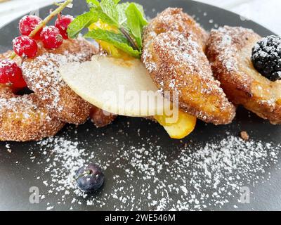 Apfelfritter auf dunklem Teller mit Zucker und Früchten. Stockfoto