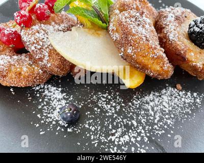 Apfelfritter auf dunklem Teller mit Zucker und Früchten. Stockfoto