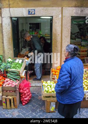 Lissabon, Portugal: 10. November 2023: Lebensmittelhändler und alte Kunden in einem typischen oder traditionellen kleinen Lebensmittelgeschäft mit Obst und Gemüse in Kartons Stockfoto