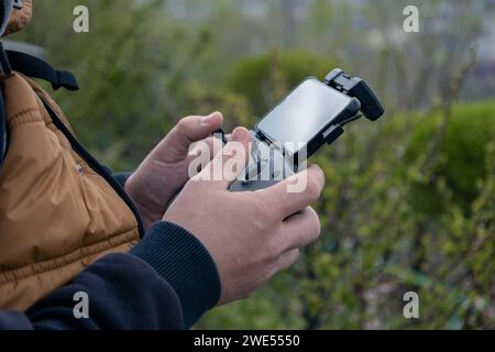 Männliche Hände halten ein Drohnenbedienfeld mit angeschlossenem Telefon, Nahaufnahme. Management durch Quadcopterflug und Videotaping von oben. Frühling im Freien. Stockfoto