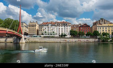 Lyon, Frankreich, 2023. Ein weißes Boot, das unter der Fußgängerbrücke des Palais de Justice segelt, mit dem Ufer des Flusses Saône im Hintergrund Stockfoto
