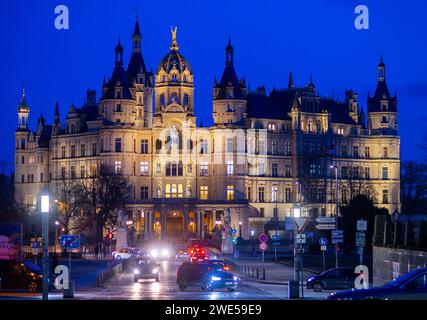 Schwerin, Deutschland. Januar 2024. Autos fahren am beleuchteten Schweriner Schloss vorbei. Die Burg war jahrhundertelang Residenz der mecklenburgischen Herzöge und Großherzöge und ist heute Sitz des landtags Mecklenburg-Vorpommern. Quelle: Jens Büttner/dpa/Alamy Live News Stockfoto