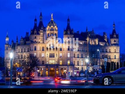 Schwerin, Deutschland. Januar 2024. Autos fahren am beleuchteten Schweriner Schloss vorbei. Die Burg war jahrhundertelang Residenz der mecklenburgischen Herzöge und Großherzöge und ist heute Sitz des landtags Mecklenburg-Vorpommern. Quelle: Jens Büttner/dpa/Alamy Live News Stockfoto