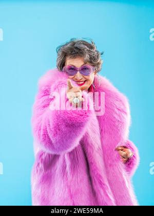 Glückliche und lustige ältere Frau, die anziehende Kleidung auf buntem Hintergrund trägt - modernes cooles Großmutterporträt, Konzepte über ältere und Stockfoto