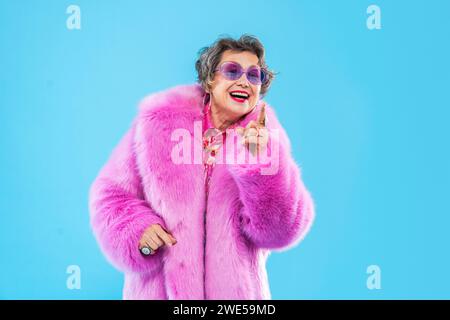 Glückliche und lustige ältere Frau, die anziehende Kleidung auf buntem Hintergrund trägt - modernes cooles Großmutterporträt, Konzepte über ältere und Stockfoto