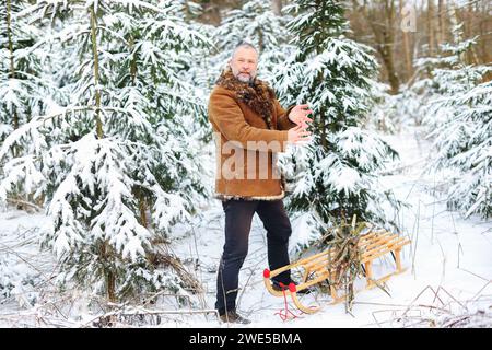 Ein Mann stapelt Feuerholz auf einen Schlitten im Winterwald Stockfoto
