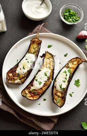 Gebackene Aubergine mit Knoblauch-Joghurt-Dressing auf Teller auf dunklem Hintergrund. Nahansicht Stockfoto